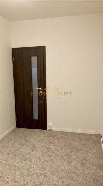 Pokoj v 3-pokojovém bytě s kobercovou podlahou a tmavými dveřmi.