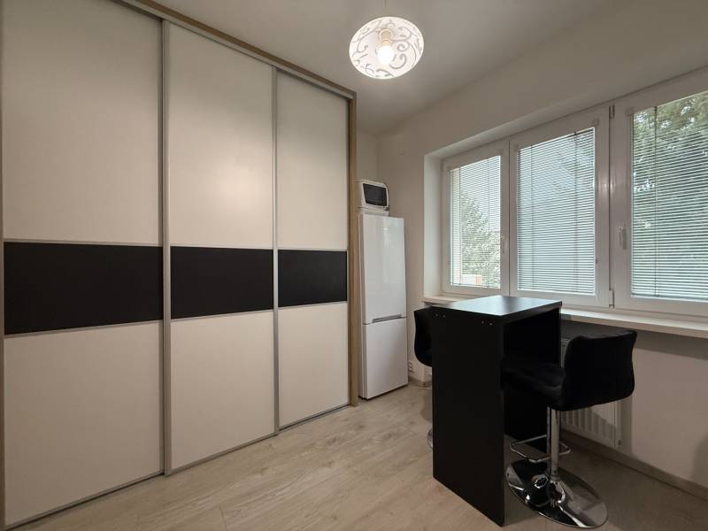 Zařízení 1-pokojového bytu, posuvná skříň, vysoká lednička, stůl se dvěma židlemi.