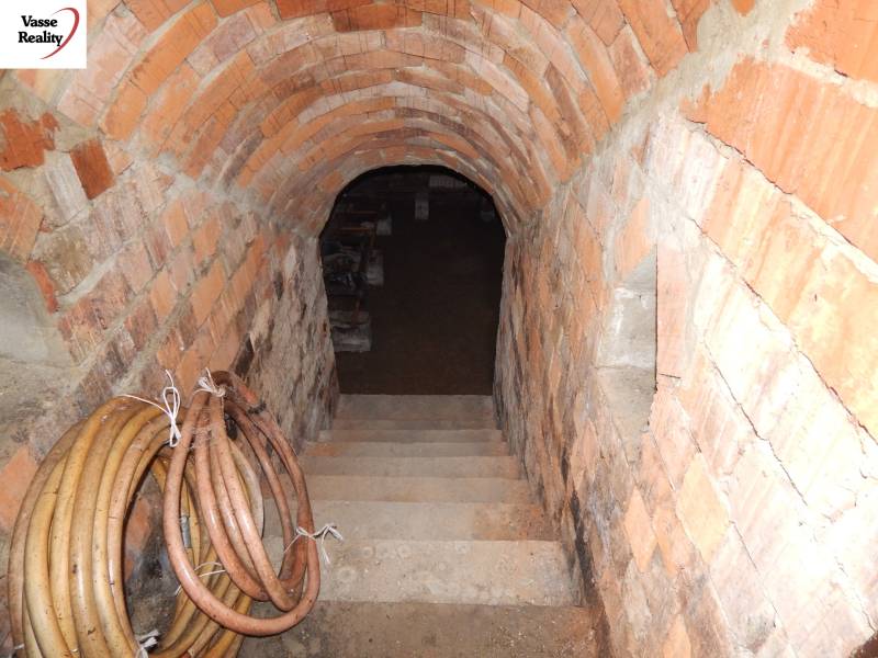 Cihlový sklep pod rodinným domem s dolů vedoucími schody a srolovanými hadicemi na stěně.