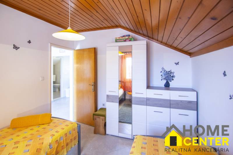 Ložnice v rekreačním apartmánu s barevným povlečením, skříňkou a dekoracemi na stěně.