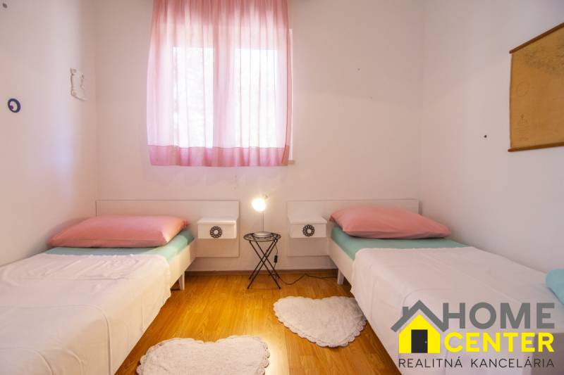 Světlá ložnice s dvěma postelemi, růžovými závěsy a podlahou s dřevěným dekorem.