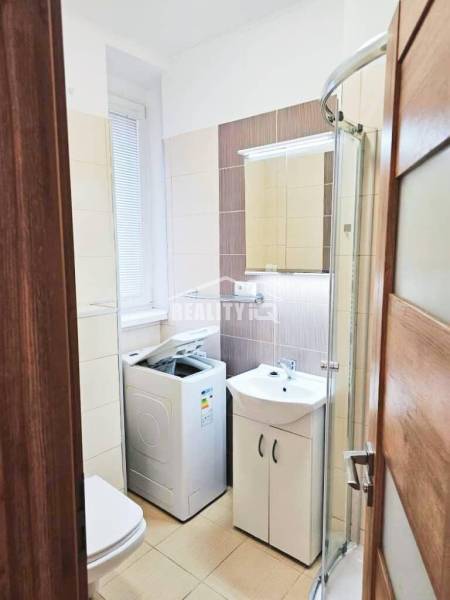 Koupelna v garsonce s pračkou, sprchovým koutem a umyvadlem.