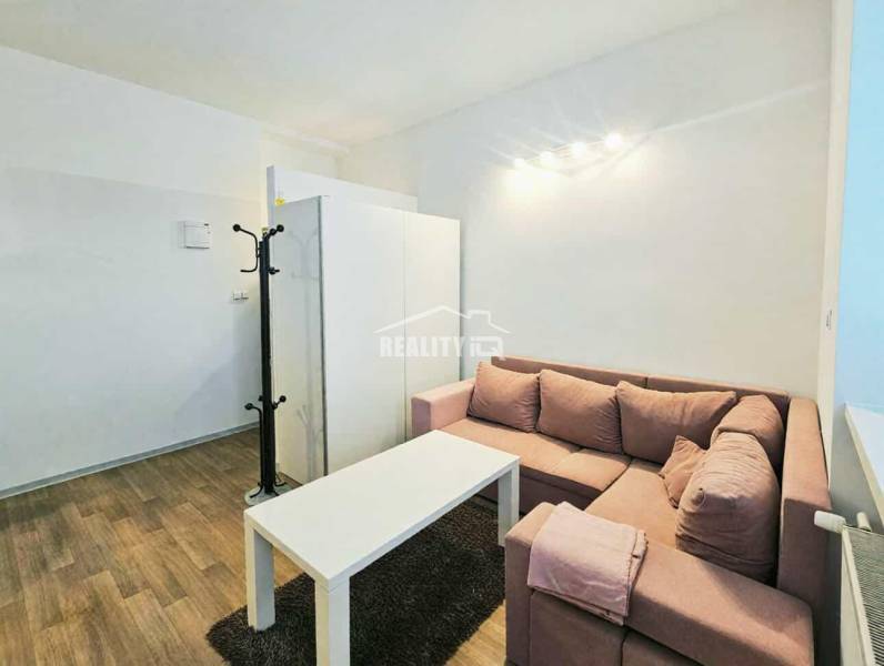 Garsonka s rohovou sedačkou, bílým stolkem a podlahou s dřevěným dekorem.