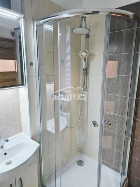 Koupelna se zaskleným sprchovým koutem a světlými dlaždicemi v garsonce.