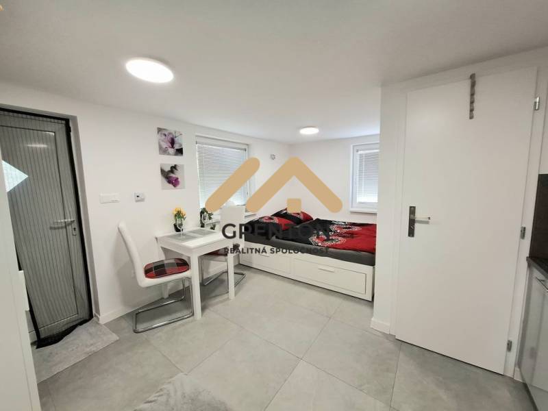 Interiér chaty s jídelním stolem, židlemi a postelí na světlé podlaze.