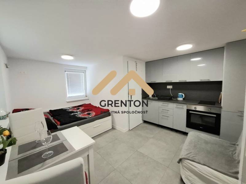 Kuchyňský kout a lůžko v chatě s obkladem šedé barvy a vybavením.