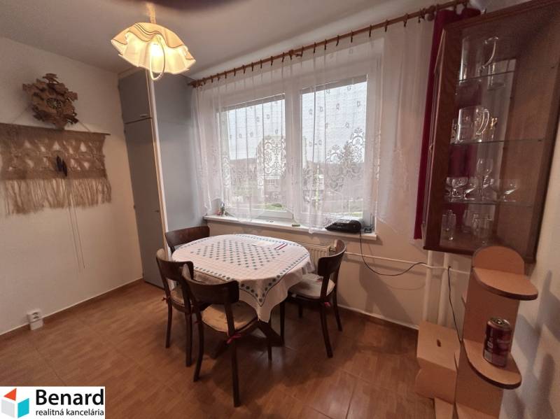 Jídelní kout v 2-pokojovém bytě s podlahou s dřevěným dekorem, stůl, židle, závěsy.