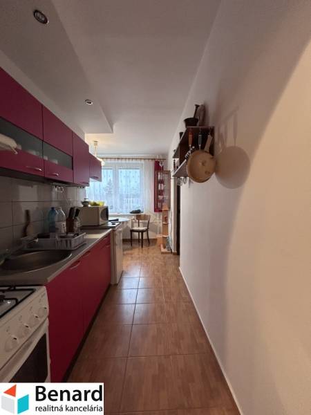 Kuchyně v 2-pokojovém bytě s podlahou s dřevěným dekorem, s jídelním koutem v pozadí.