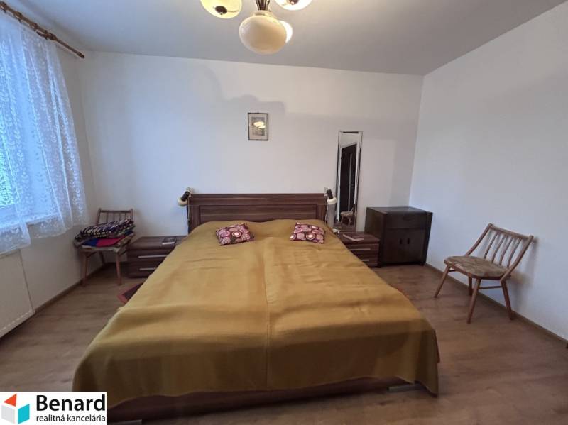 Ložnice v 2pokojovém bytě s postelí, židlemi a podlahou s dřevěným dekorem.