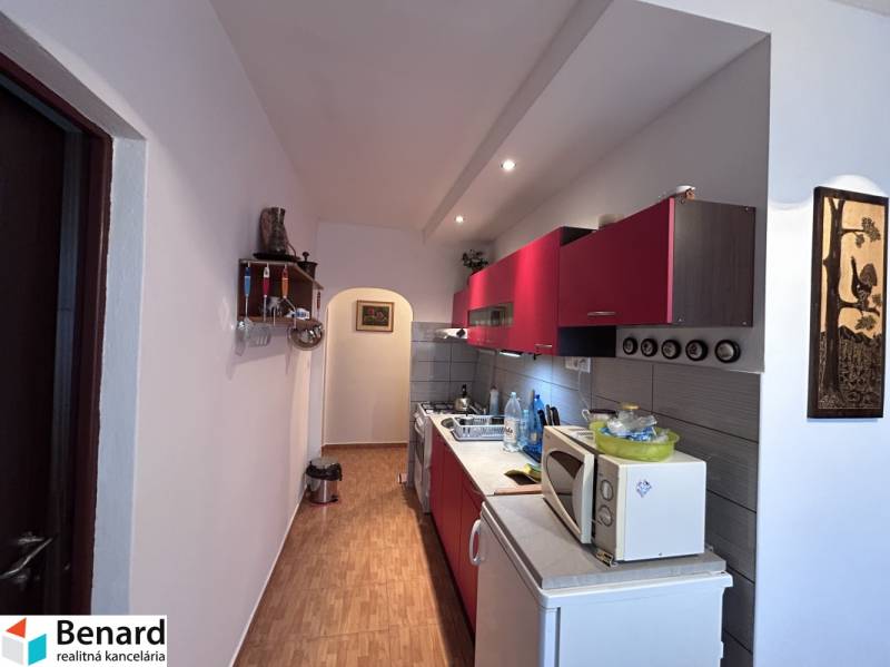 Kuchyně s červenými skříňkami a podlahou s dřevěným dekorem v 2pokojovém bytě.