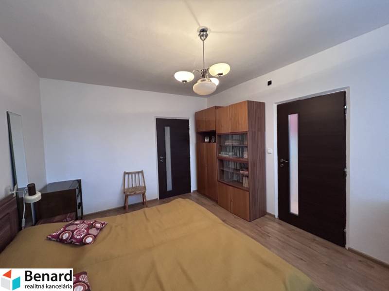 Ložnice v 2-pokojovém bytě s postelí, skříní a podlahou s dřevěným dekorem.