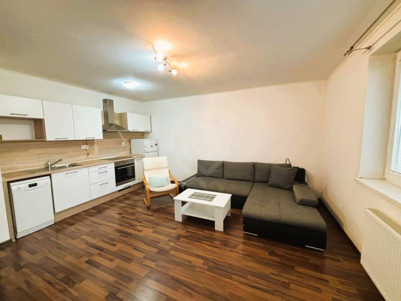 Obývací pokoj v 2-pokojovém bytě s rohovou sedačkou a kuchyňskou linkou.