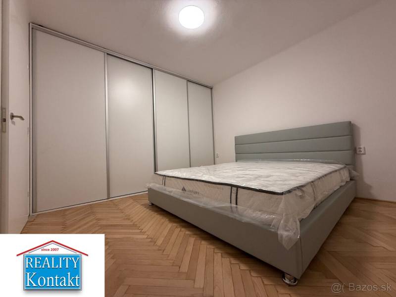 Ložnice v 2pokojovém bytě s podlahou s dřevěným dekorem a velkou vestavěnou skříní.