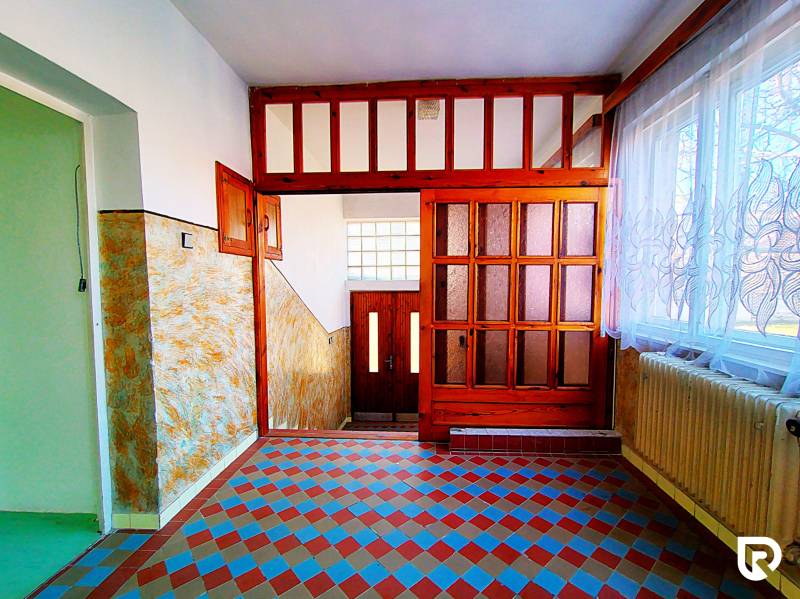 Chodba v rodinném domě s dlažbou s barevným vzorem, dřevěnými dveřmi a záclonami.