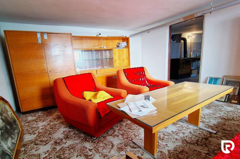 Obývací pokoj v rodinném domě se staršími křesly, stolem a prosklenou skříní.