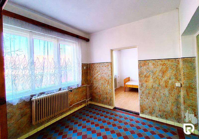 Interiér rodinného domu s dlažbou, radiátorem a oknem se záclonou.