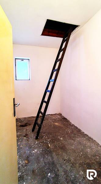Půda v rodinném domě s žebříkem vedoucím do stropního otvoru.