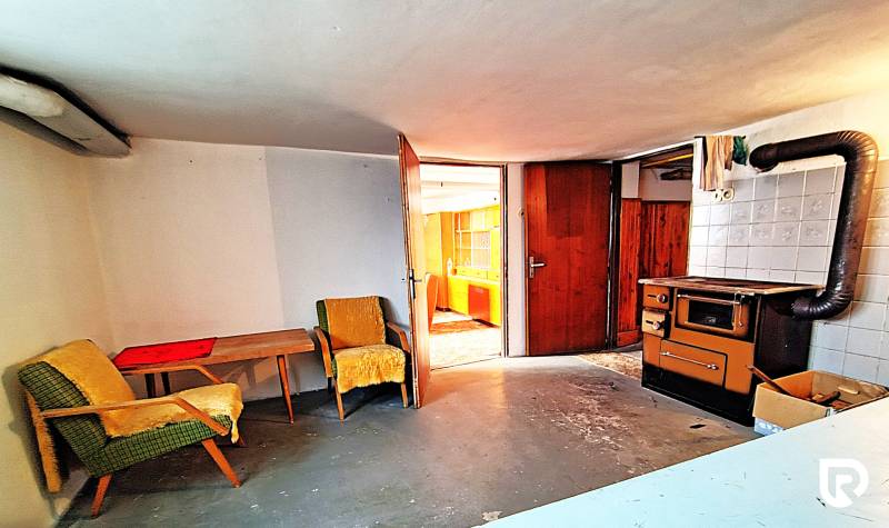 Pokoj v rodinném domě s křesly, stolem a starými kamny.