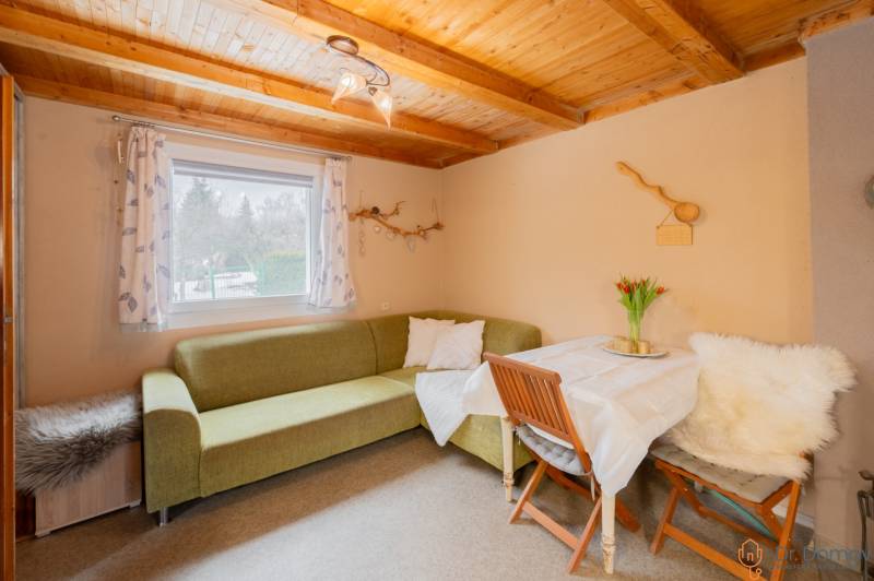 Interiér chaty s rohovou sedačkou, stolem a dřevěným stropem.