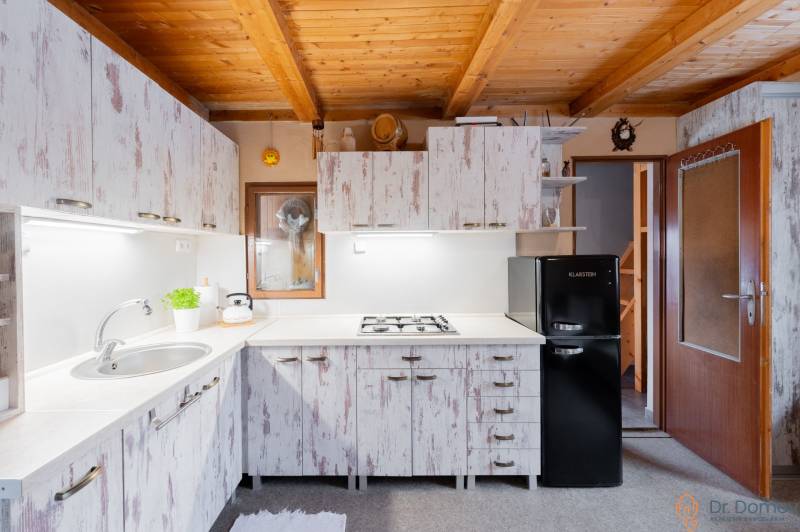 Kuchyně v chatě s dřevěným stropem a vintage skříněmi, útulné vybavení.