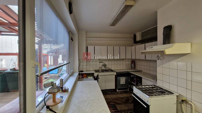 Kuchyně v rodinném domě se spotřebiči, dlaždicemi a oknem s výhledem na terasu.