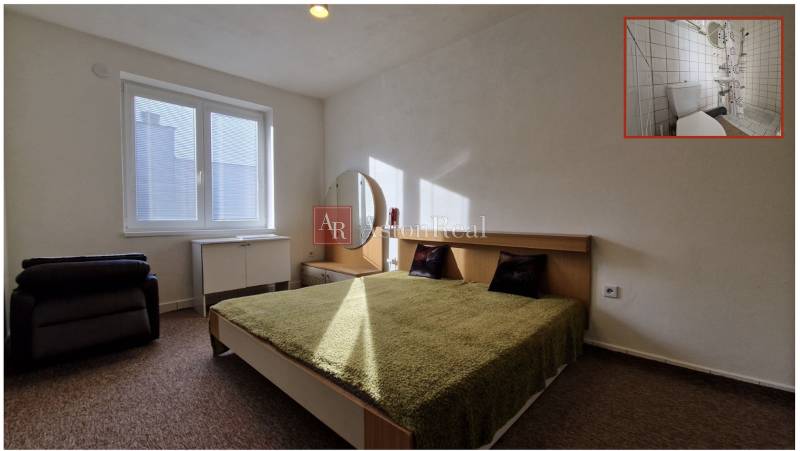 Ložnice s manželskou postelí, zelenou přikrývkou, nočním stolkem a zrcadlem v rodinném domě.