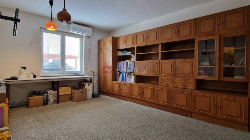 Rodinný dům má pracovnu s dřevěnou policovou stěnou, velkým stolem a kobercovou podlahou.