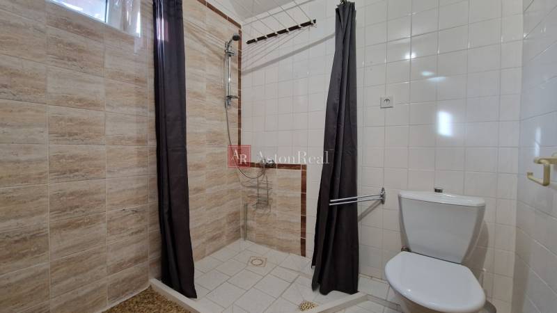 Koupelna v rodinném domě s jednoduchým sprchovým koutem a světlými obklady.