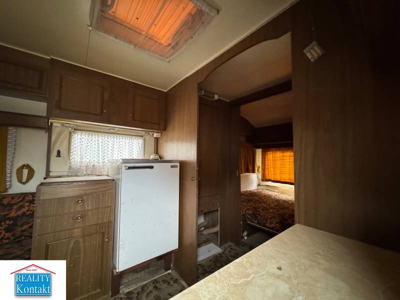 Interiér s podlahou s dřevěným dekorem, kuchyňskou linkou a postelí v Pozemky - bydlení.