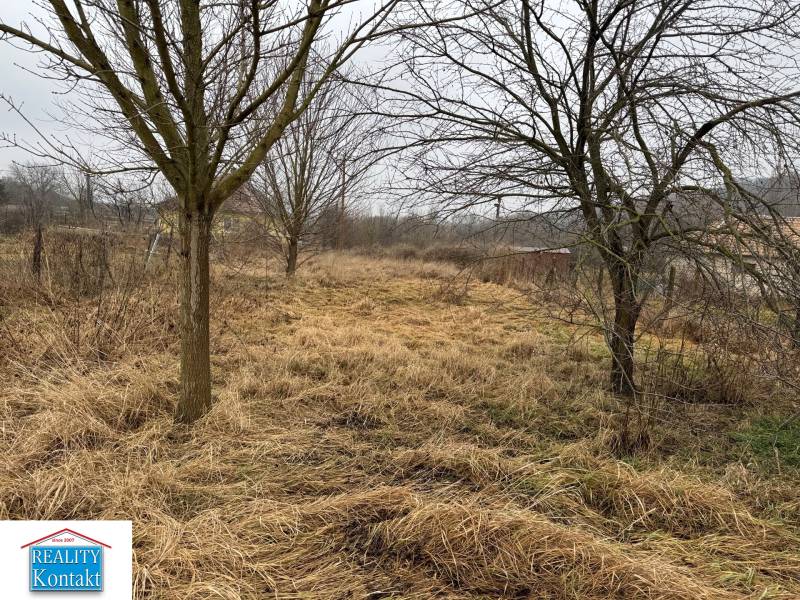 Pozemek na bydlení v Dubníku na Dubnícké ulici, obklopený stromy a travnatým porostem.