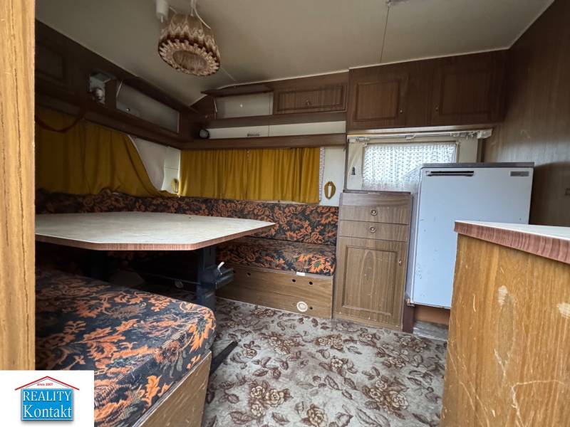 Interiér obytného prostoru s kobercovou podlahou, sedací soupravou a stolem.