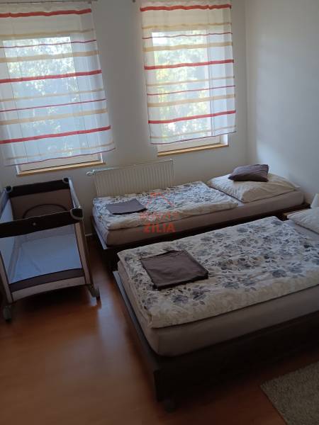 Dětská postýlka a dvě postele v ložnici s podlahou s dřevěným dekorem.