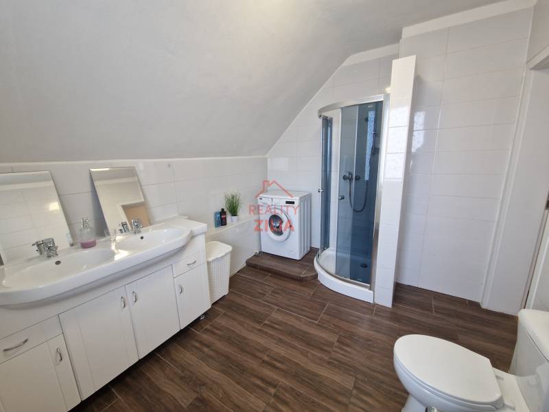 Koupelna v rodinném domě s umyvadlem, sprchovým koutem a podlahou s dřevěným dekorem.