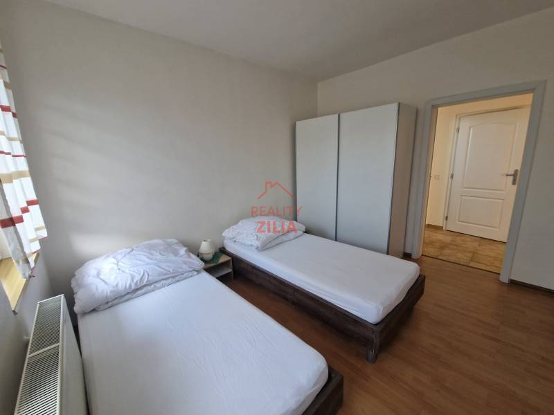 Pokoj v rodinném domě s dvěma postelemi, skříní a podlahou s dřevěným dekorem.