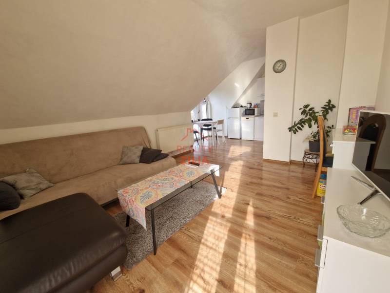 Podkrovní obývací pokoj v rodinném domě s pohovkou, jídelním stolem a podlahou s dřevěným dekorem.