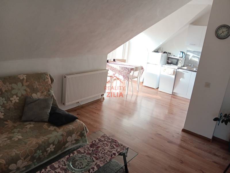 Podkrovní prostor v rodinném domě s kuchyní, květinovou pohovkou a podlahou s dřevěným dekorem.