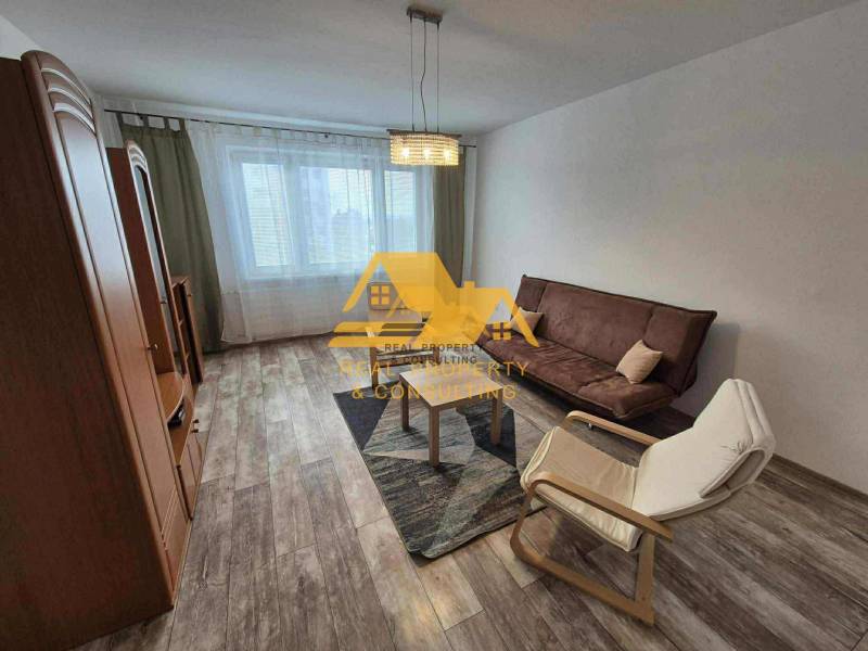 Obývací pokoj v 3-pokojovém bytě s pohovkou, křeslem a podlahou s dřevěným dekorem.