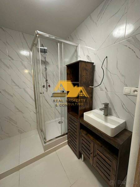 Koupelna v 2-pokojovém bytě s bílými dlaždicemi, sprchovým koutem a umyvadlem na skříňce.