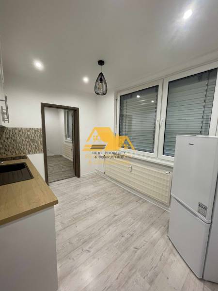 Kuchyně v 1-pokojovém bytě s podlahou s dřevěným dekorem a bílými elektrospotřebiči.