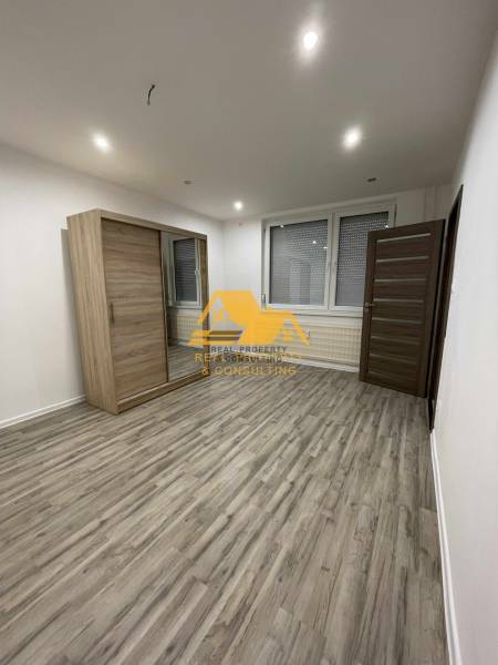 Prostorný pokoj s posuvnou skříní a podlahou s dřevěným dekorem v 1-pokojovém bytě.