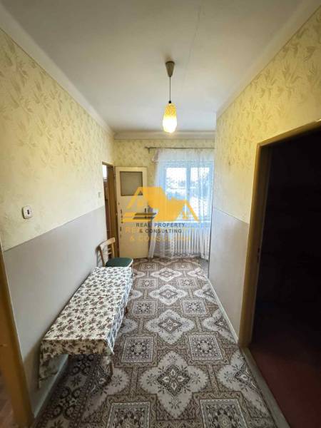 Chodba v rodinném domě s kobercovým dekorem a stolem, okno na konci místnosti.