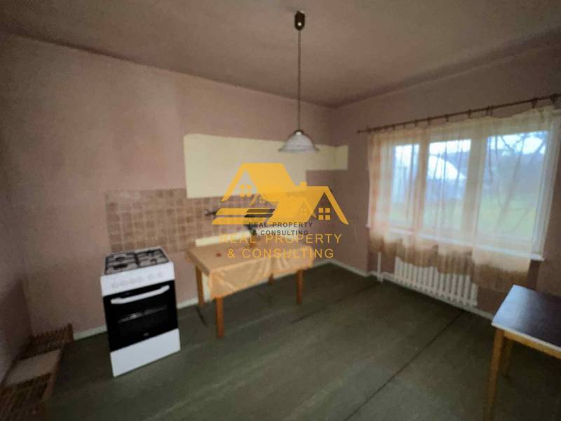 Kuchyně v rodinném domě se sporákem, stolem, záclonou a světlým dekorem stěn.