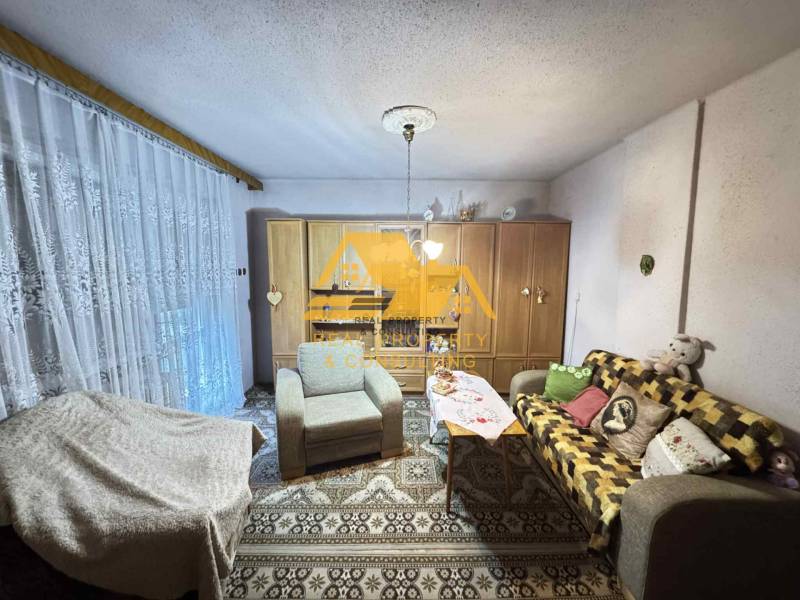 Obývací pokoj v rodinném domě s pohovkou, koberec a skříně s dekoracemi.