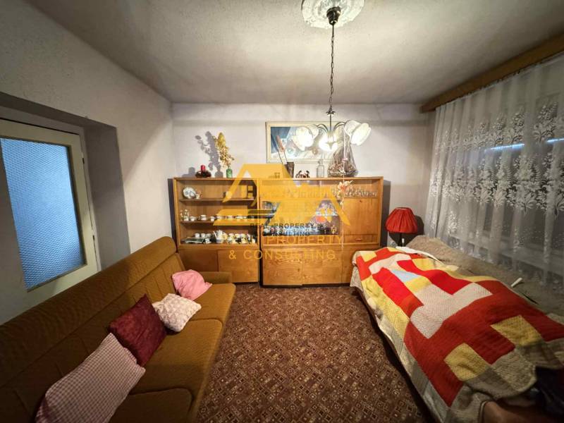 Obývací pokoj v rodinném domě s kobercem, pohovkou a skříní s porcelánem.