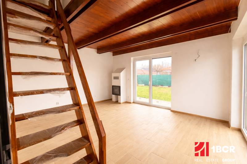 Interiér rodinného domu se schodištěm, krbem a podlahou s dřevěným dekorem.