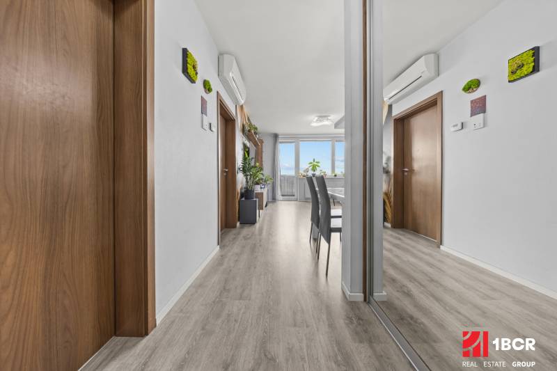 Interiér 2-pokojového bytu s podlahou s dřevěným dekorem, zrcadlem a klimatizací.