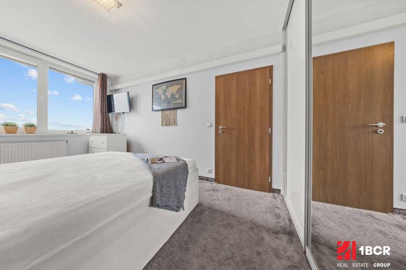 Světlá ložnice s postelí, velkým oknem a šatní skříní v 2pokojovém bytě.