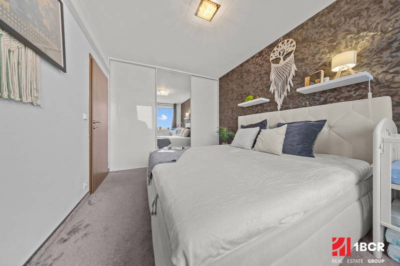 Ložnice v 2pokojovém bytě s manželskou postelí, zrcadlovou skříní a dekoracemi na stěně.