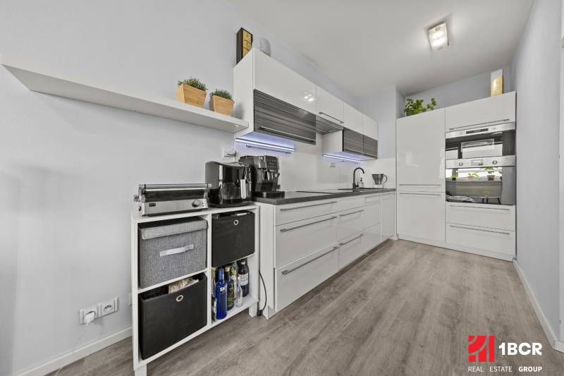 Kuchyně v 2-pokojovém bytě s bílými skříňkami a podlahou s dřevěným dekorem.