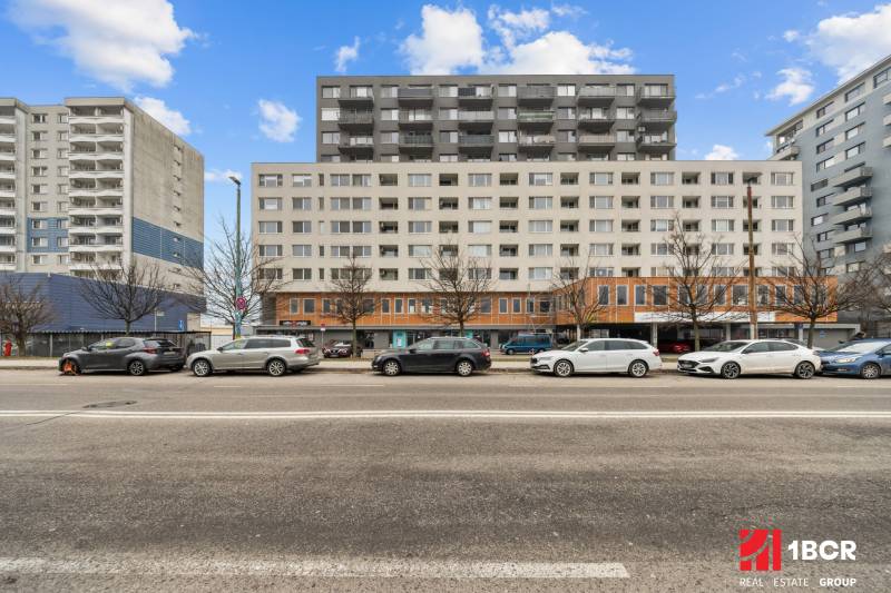 Budova na ulici Budatinská v Bratislavě - Petržalce s auty zaparkovanými před ní.